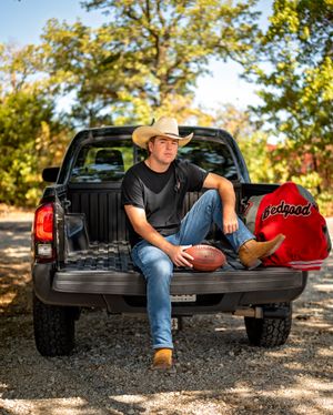 Casual senior portrait with football and cowboy hat in pickup truck bed on sunny day.