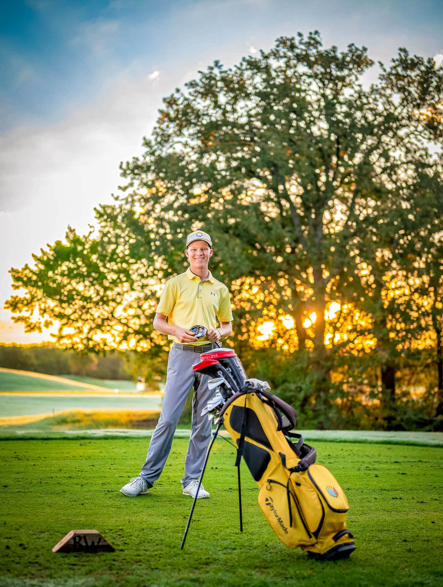 Teen Golfer posing with yellow golf bag on course at sunset.
