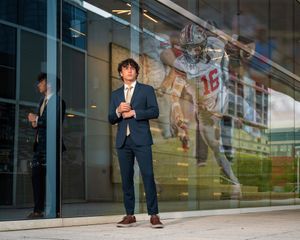 Young man in navy suit stands before glass building reflecting a football player graphic.