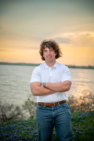 Lakeside sunset portrait of teenager in white polo and jeans with arms crossed among bluebonnets.