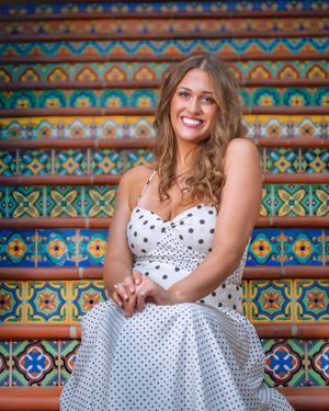 Smiling woman in white polka dot dress sitting on colorful mosaic tiled steps outdoors.