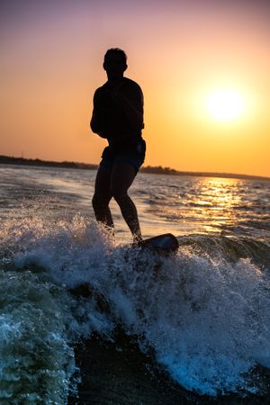 Silhouette of a teen surfer riding a wave during golden sunset over water.