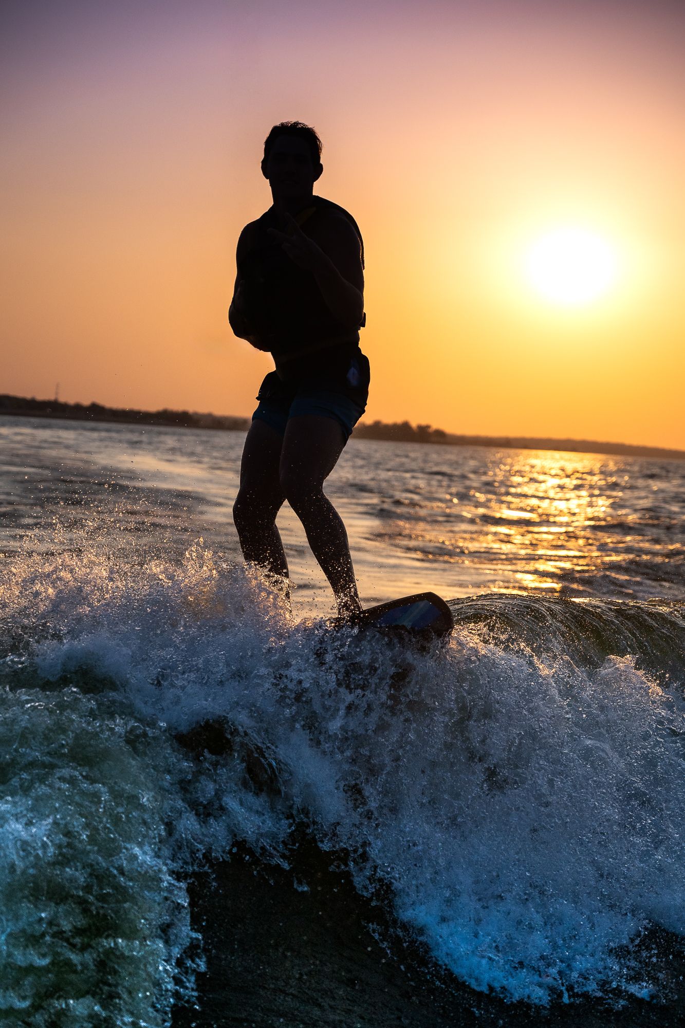 Silhouette of a teen surfer riding a wave during golden sunset over water.