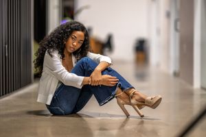 A senior teenager in white top and jeans sits casually on the floor wearing brown heels.