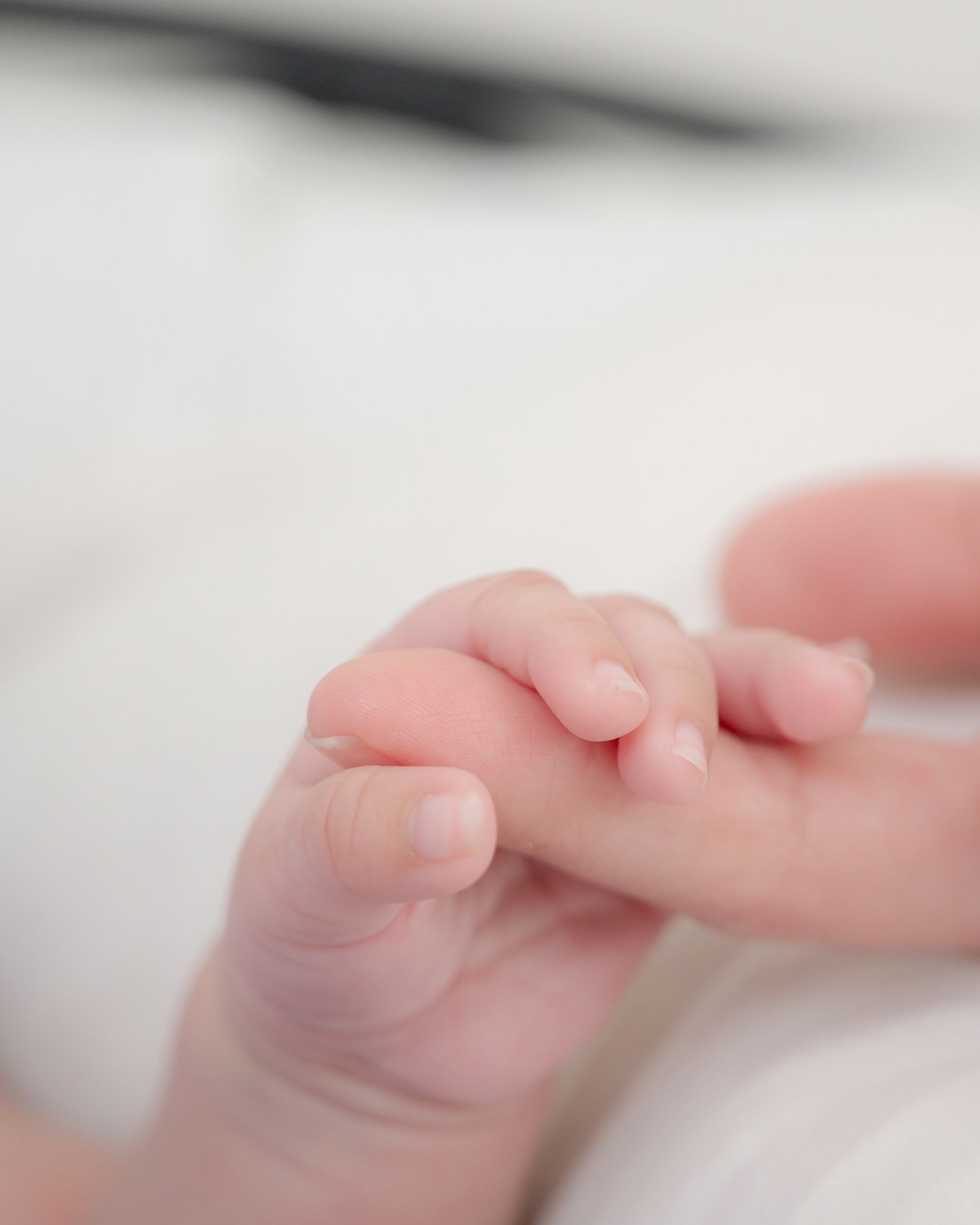 Close-up of tiny baby hand with delicate fingers against white background.