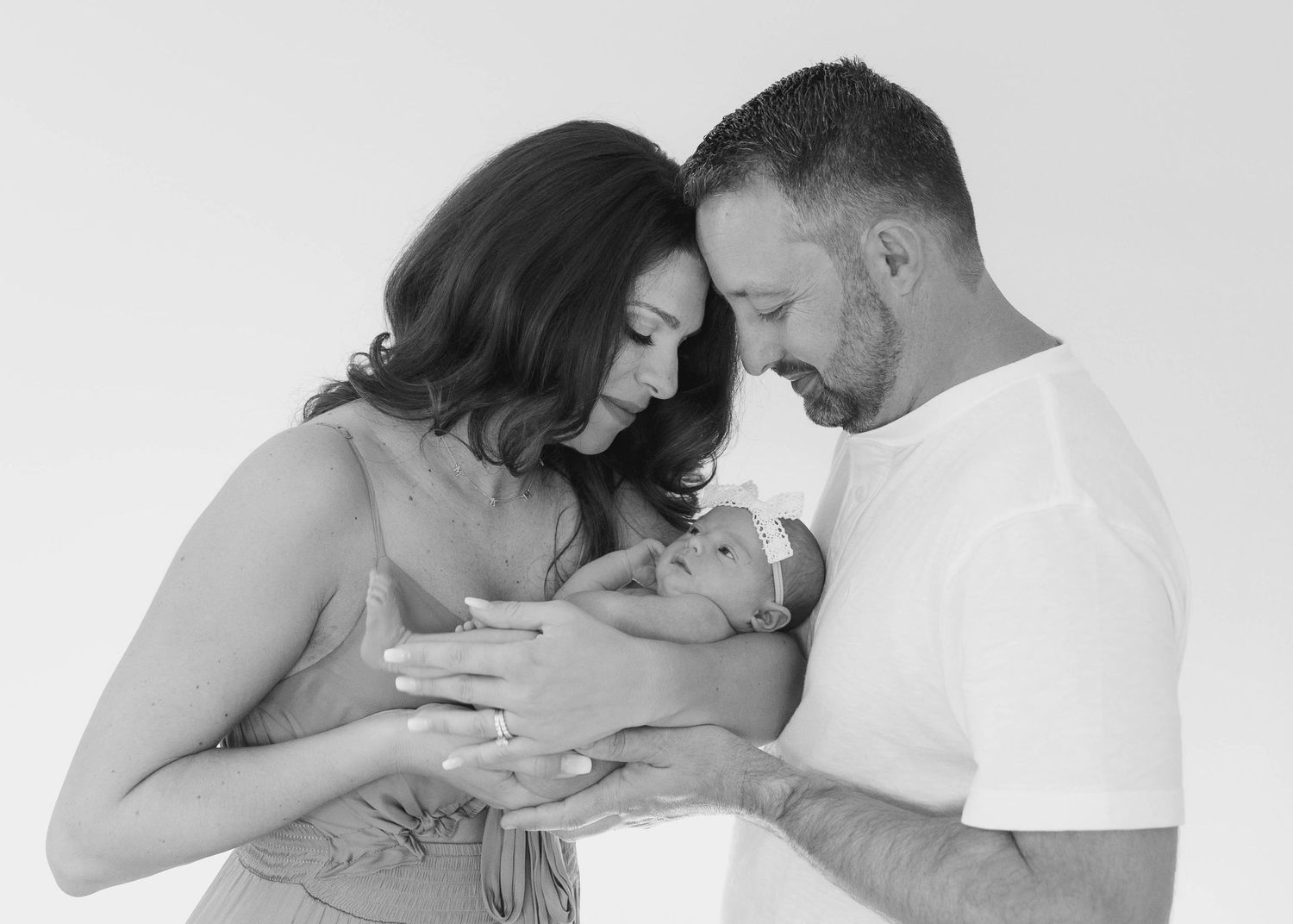 An intimate black and white portrait of parents gazing lovingly at their sleeping newborn baby.