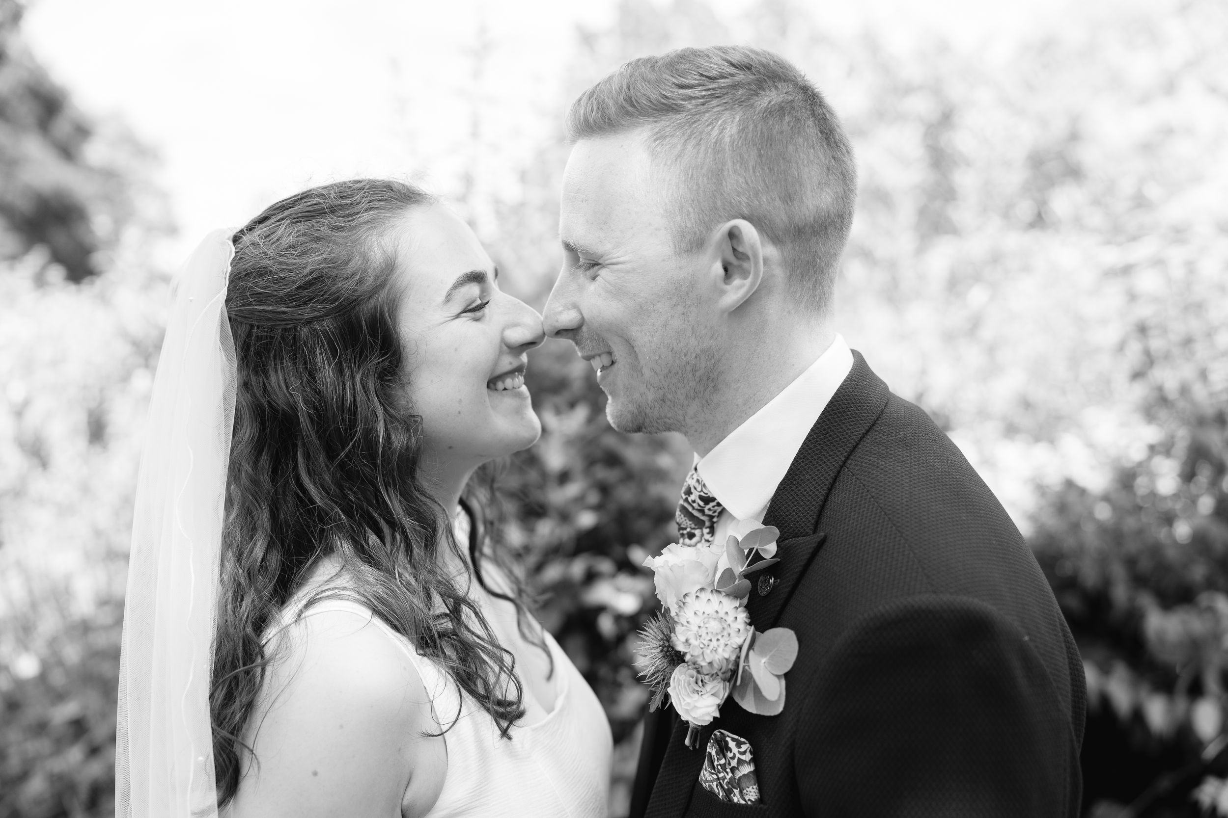 Black and white wedding photo of smiling bride and groom sharing a joyful moment outdoors.