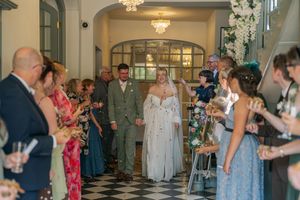 Bride and groom walk through confetti-throwing guests in elegant venue during wedding ceremony exit.