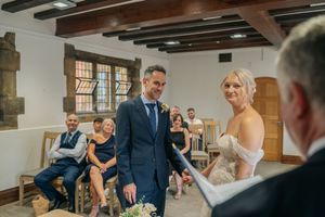 Bride and groom smiling during intimate wedding ceremony in rustic venue with wooden beams and seated guests.