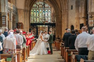Bride and groom exchange vows at the altar of a grand Gothic church with stained glass windows.