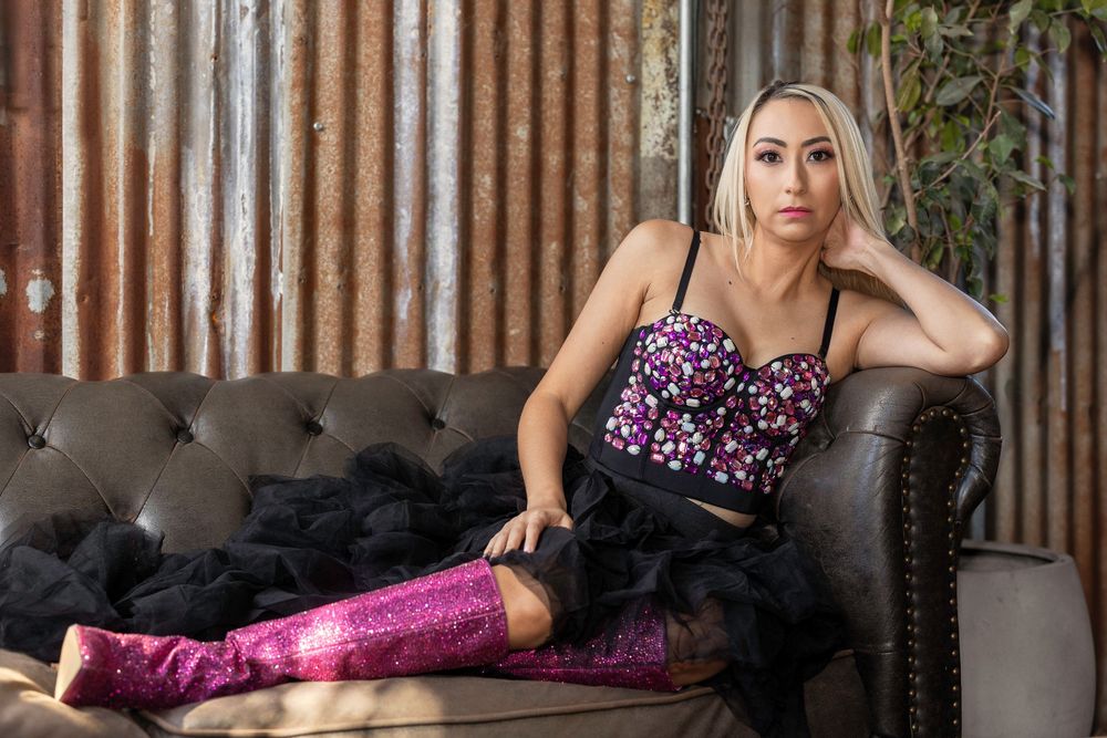 A glamorous boudoir photoshoot featuring a model in pink sequins and black tulle on a vintage sofa.