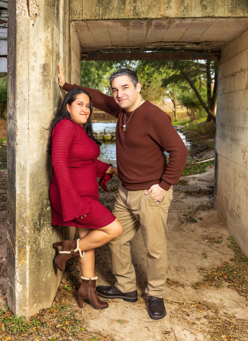 Couple embraces under concrete archway wearing red sweater and brown top.