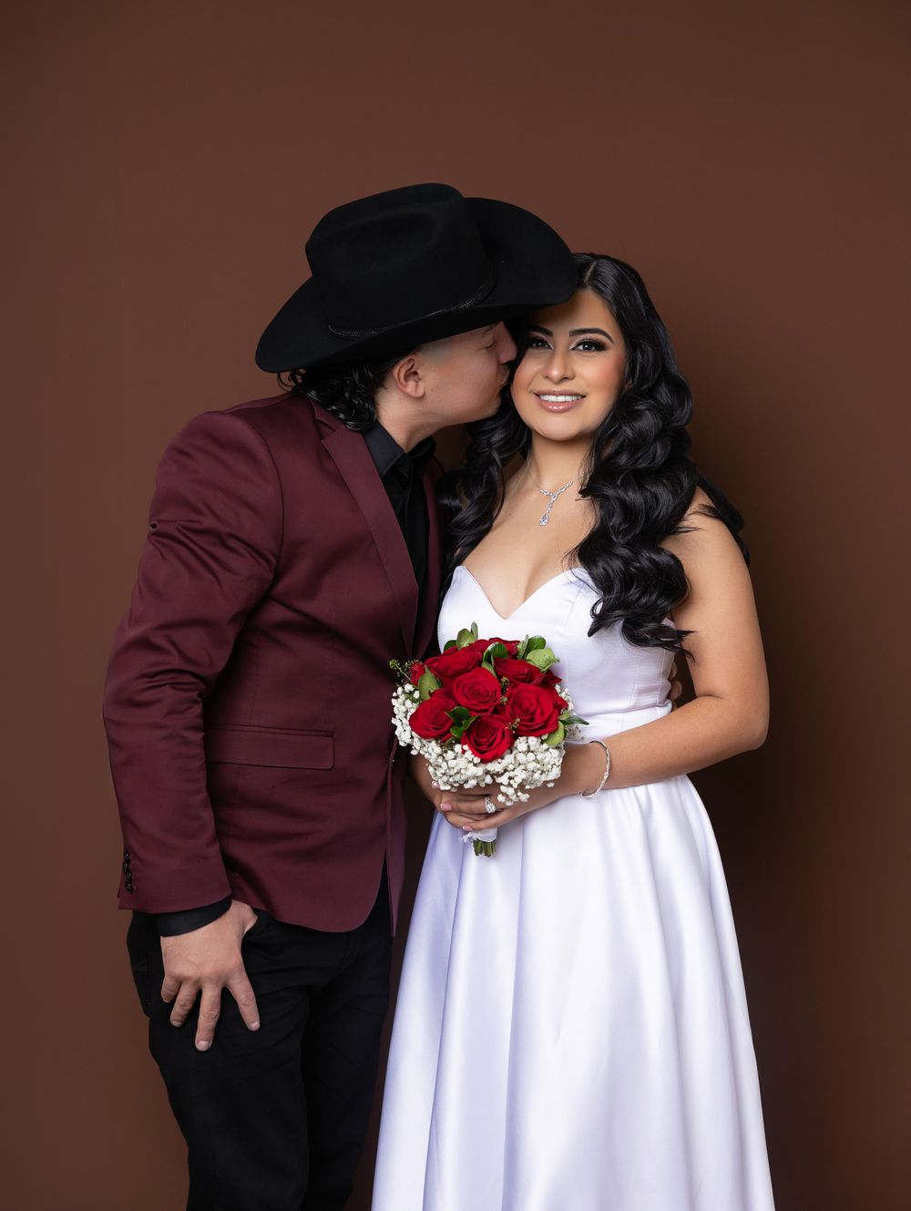 A romantic portrait with red roses against a brown backdrop featuring western formal attire.