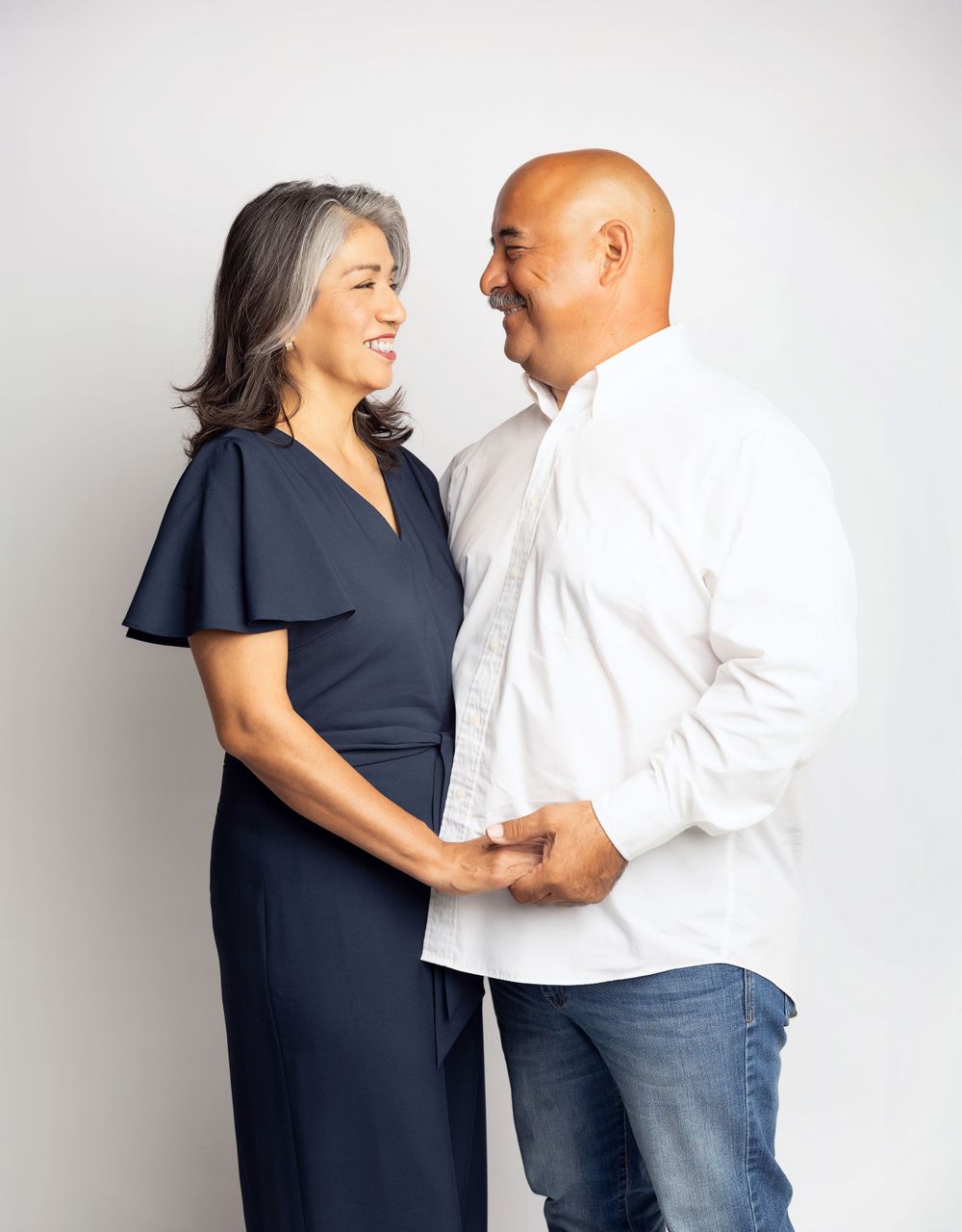 A couple sharing a tender moment while dressed in navy and white against a light background.