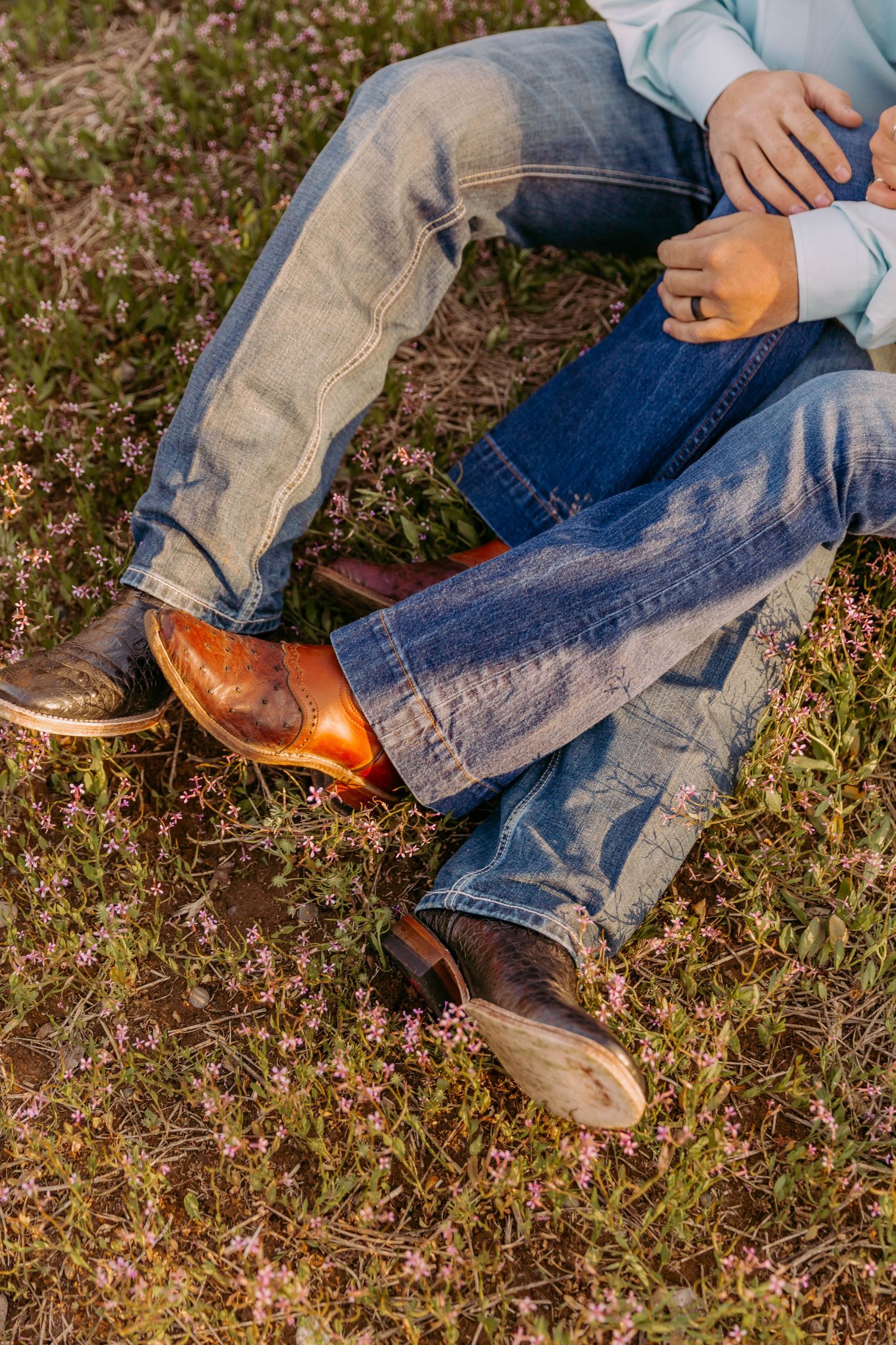 Weathered cowboy boots and denim jeans shown in close-up detail on grass.