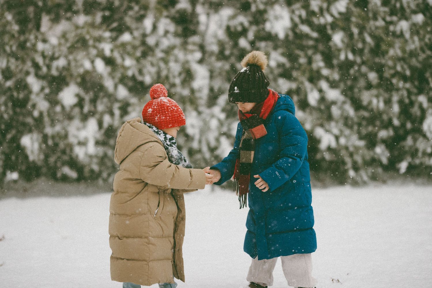 Two children in winter coats play together in a snowy winter landscape.