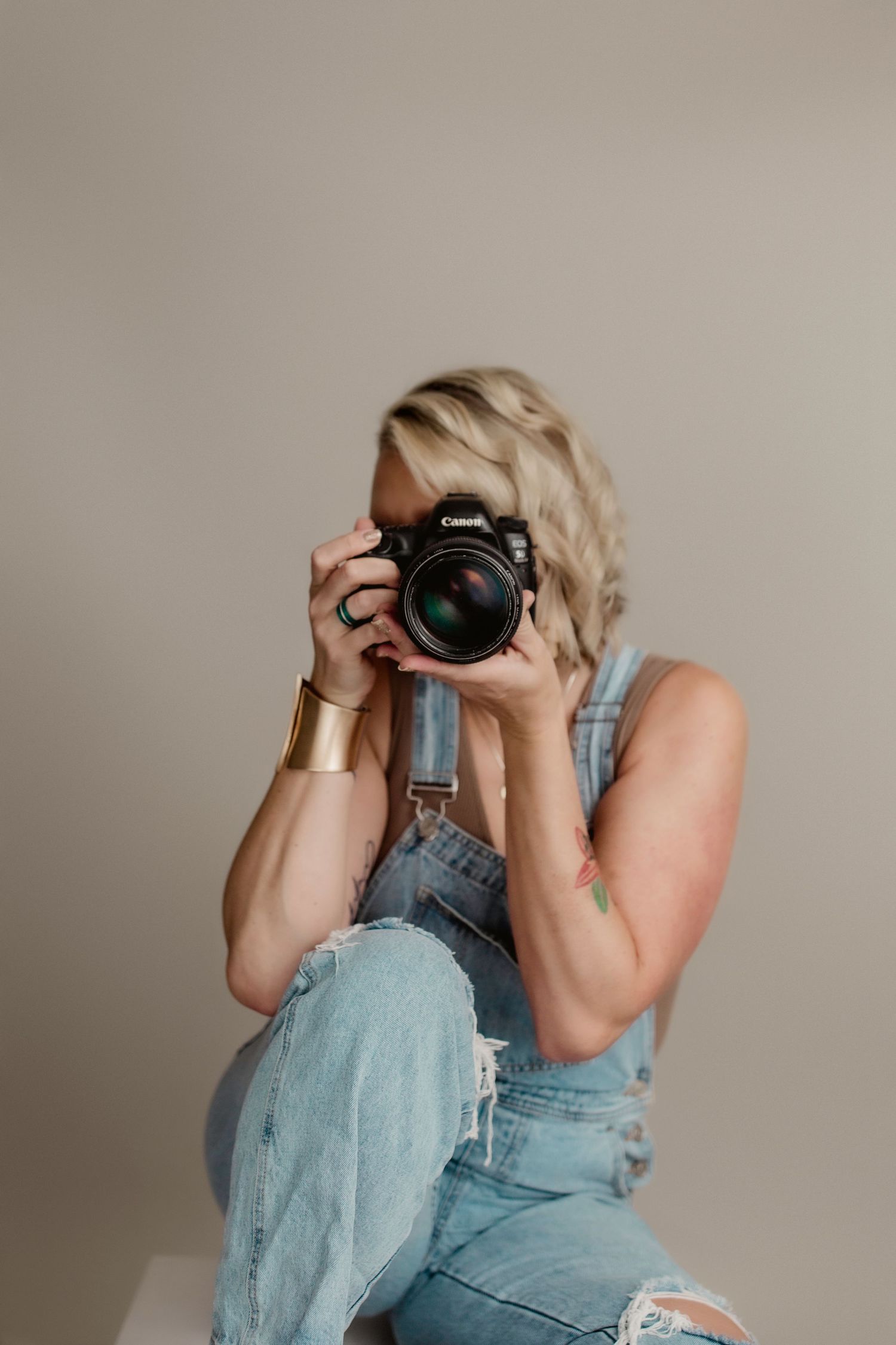 Photographer in denim overalls taking a photo with a professional DSLR camera against neutral background.