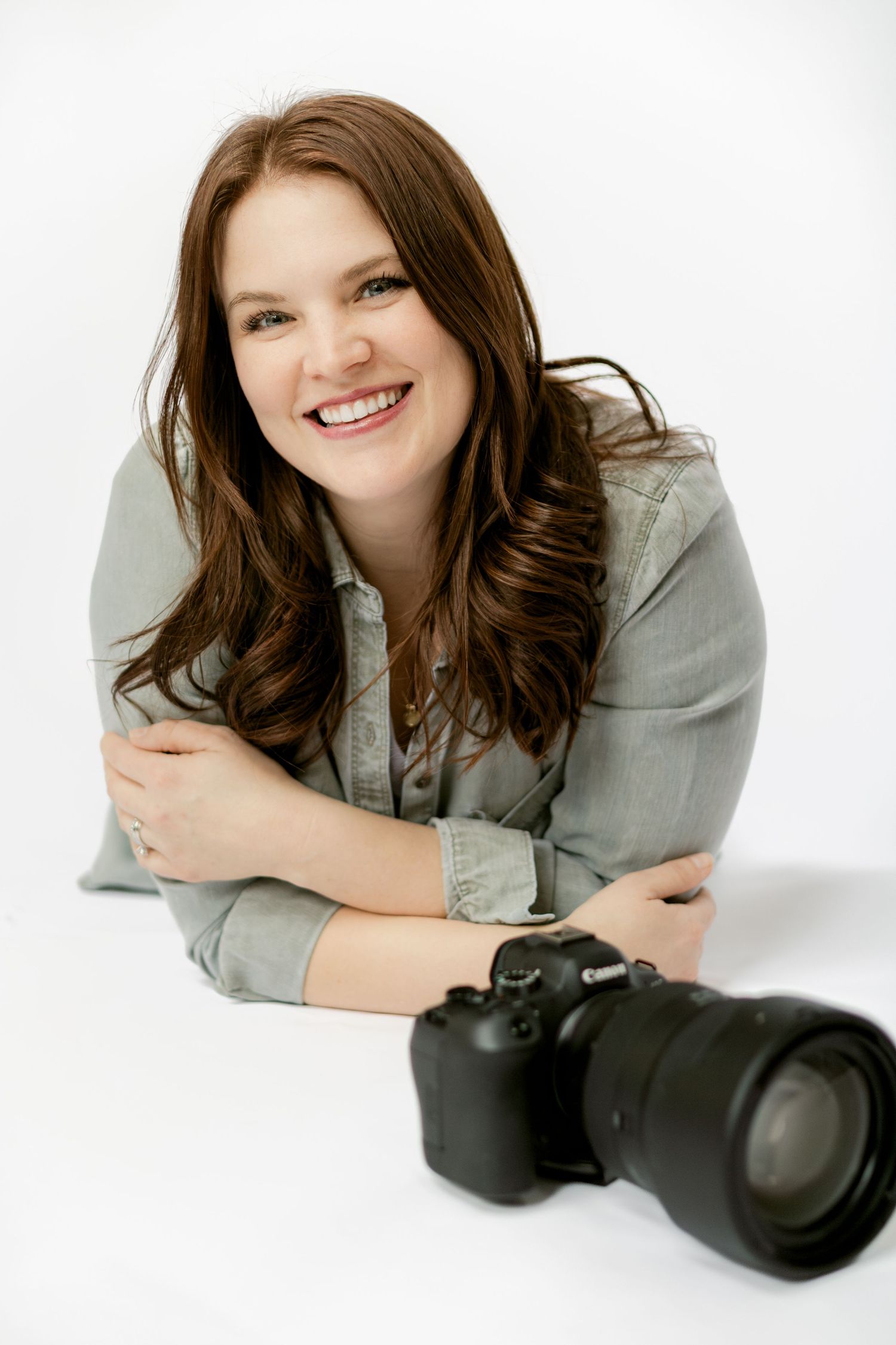A cheerful photographer holds a camera while sitting against a white backdrop.