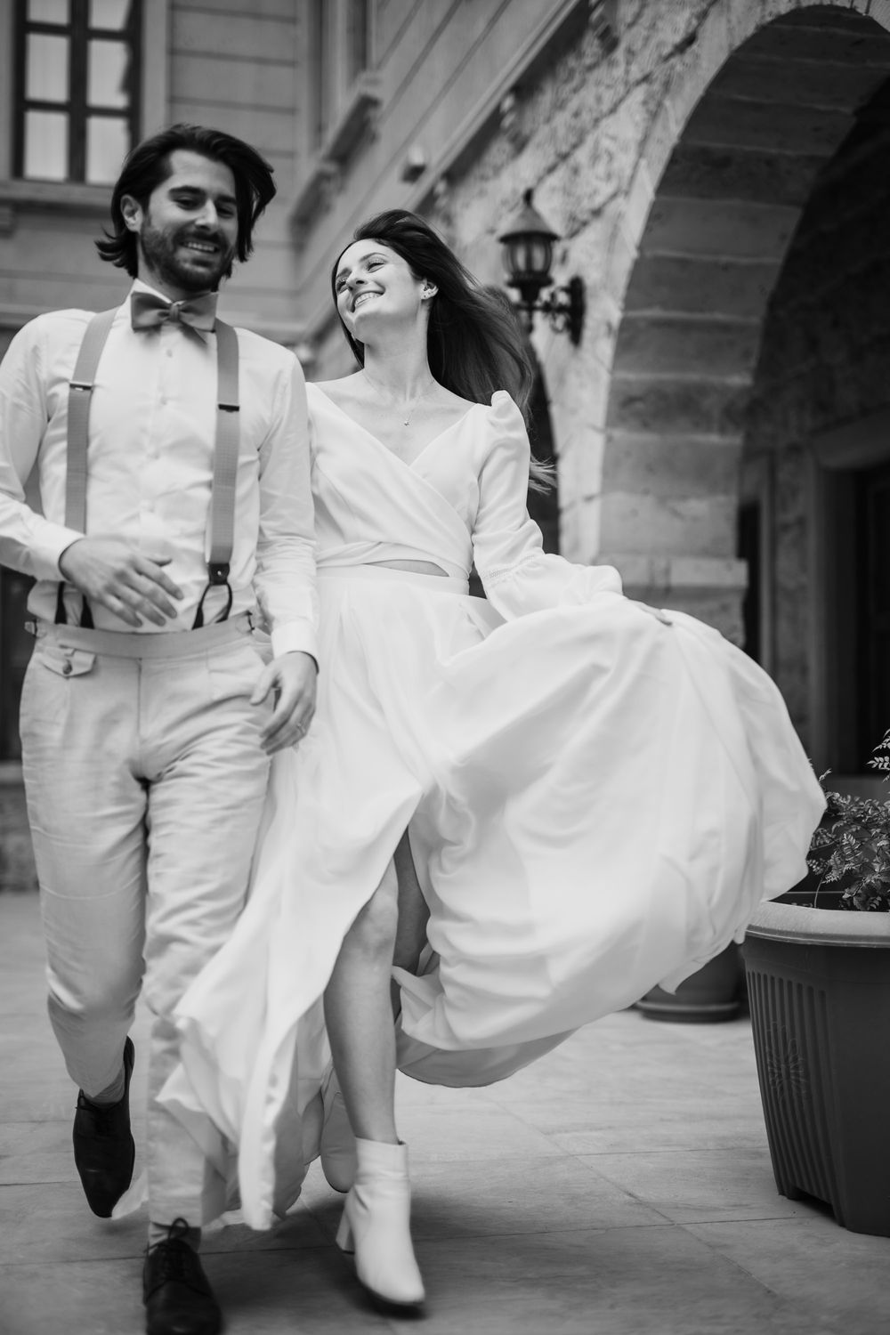 A romantic black and white photo of a loving couple in all-white wedding attire dancing together in an elegant venue.