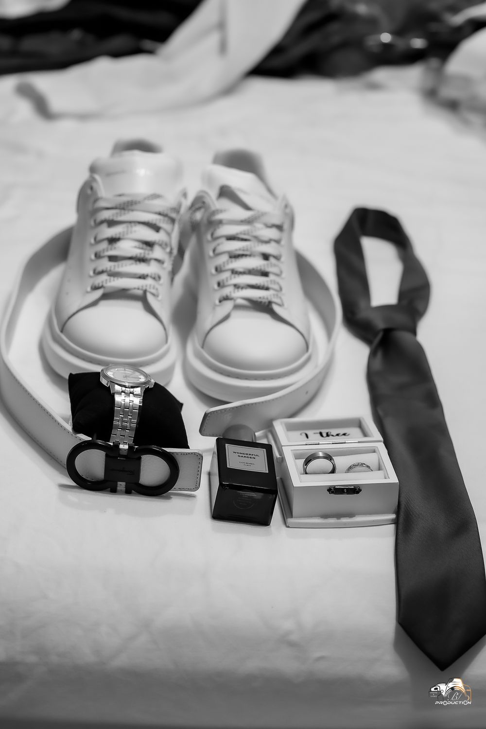 Wedding accessories including white sneakers, tie, and rings arranged on white surface.