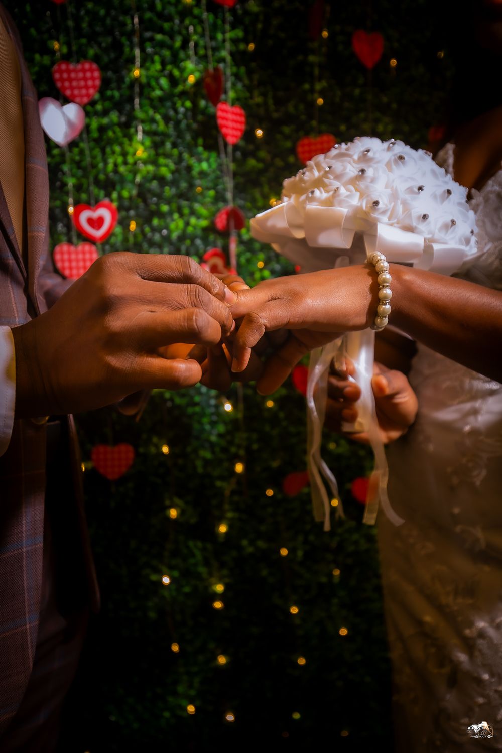 Close-up of hands exchanging rings during a wedding ceremony with heart decorations in background.