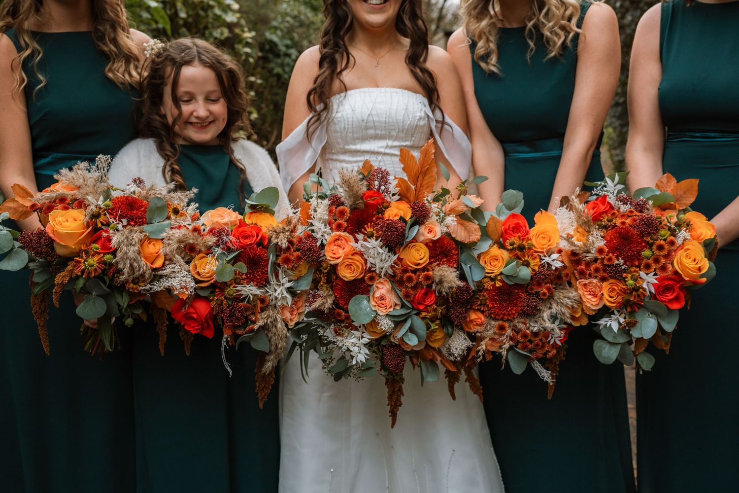 A wedding bouquet with red roses, eucalyptus leaves and coral berries sits in focus with a blurred couple in background.