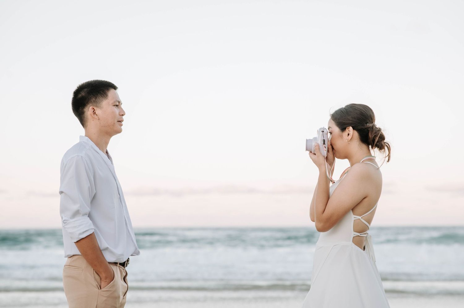 A couple captures candid moments during their beach photoshoot at dusk.