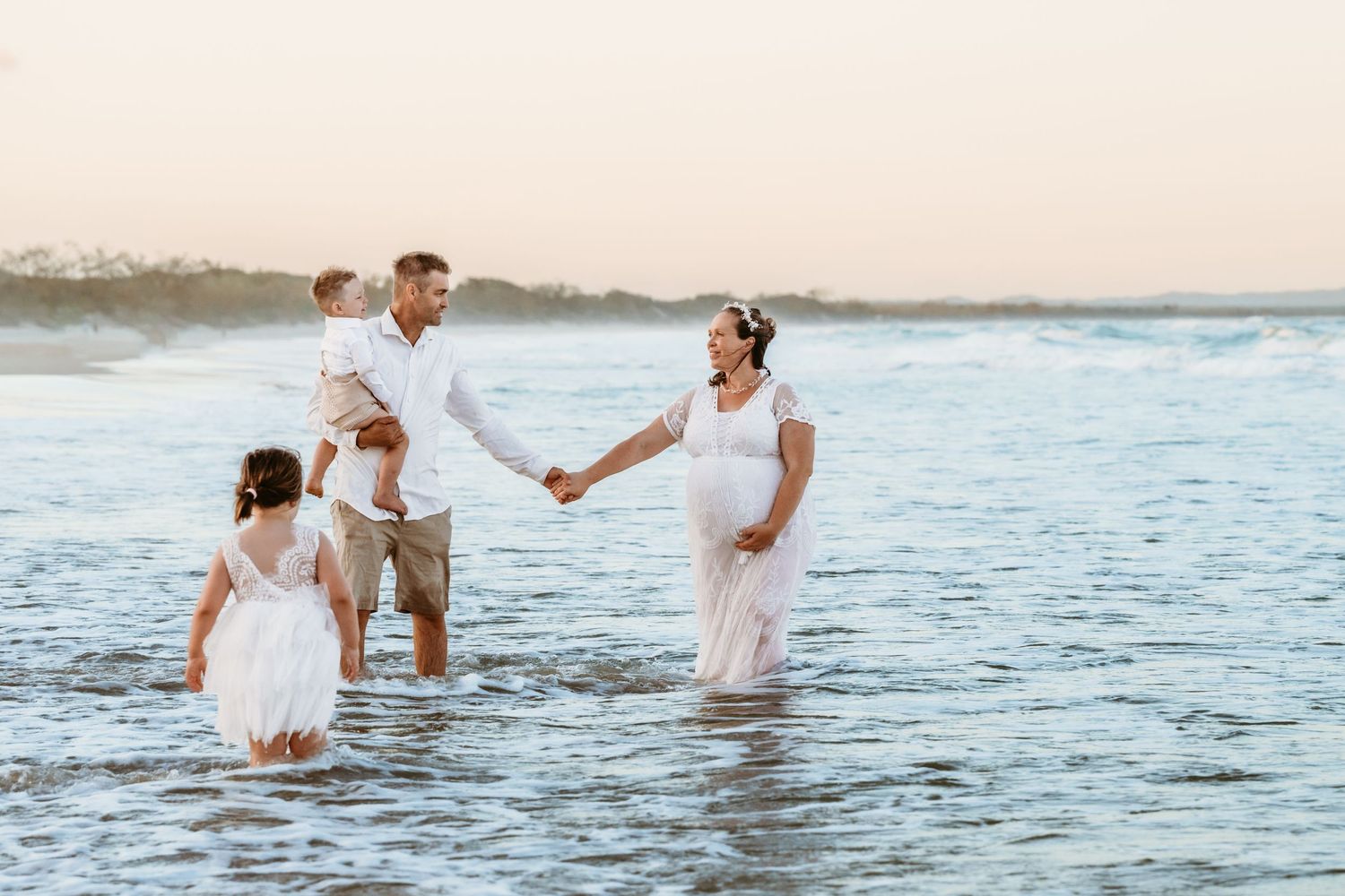 Family wading in ocean waves during sunset beach photography session.