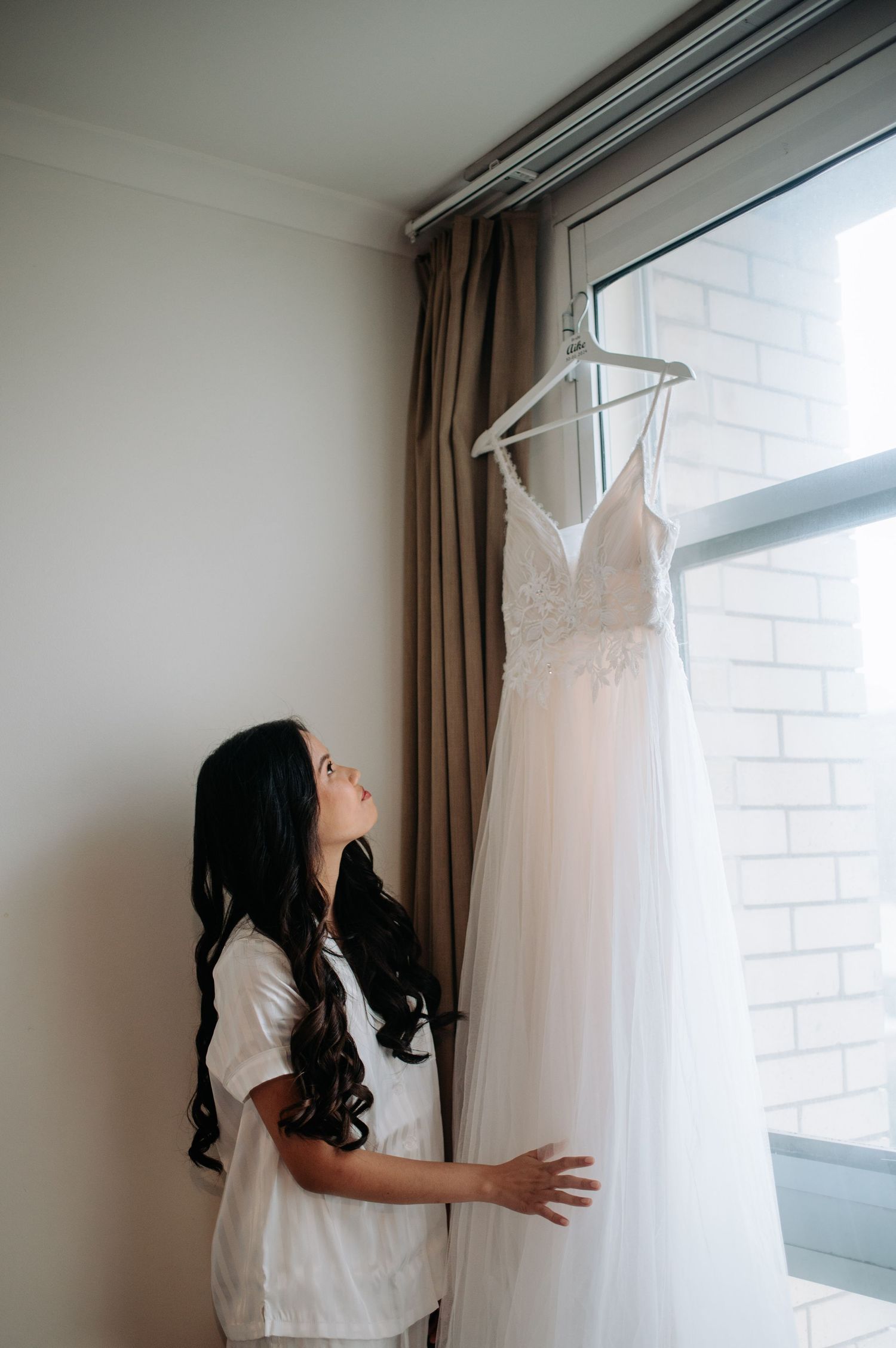 A white wedding dress hanging by a window with natural light streaming in.