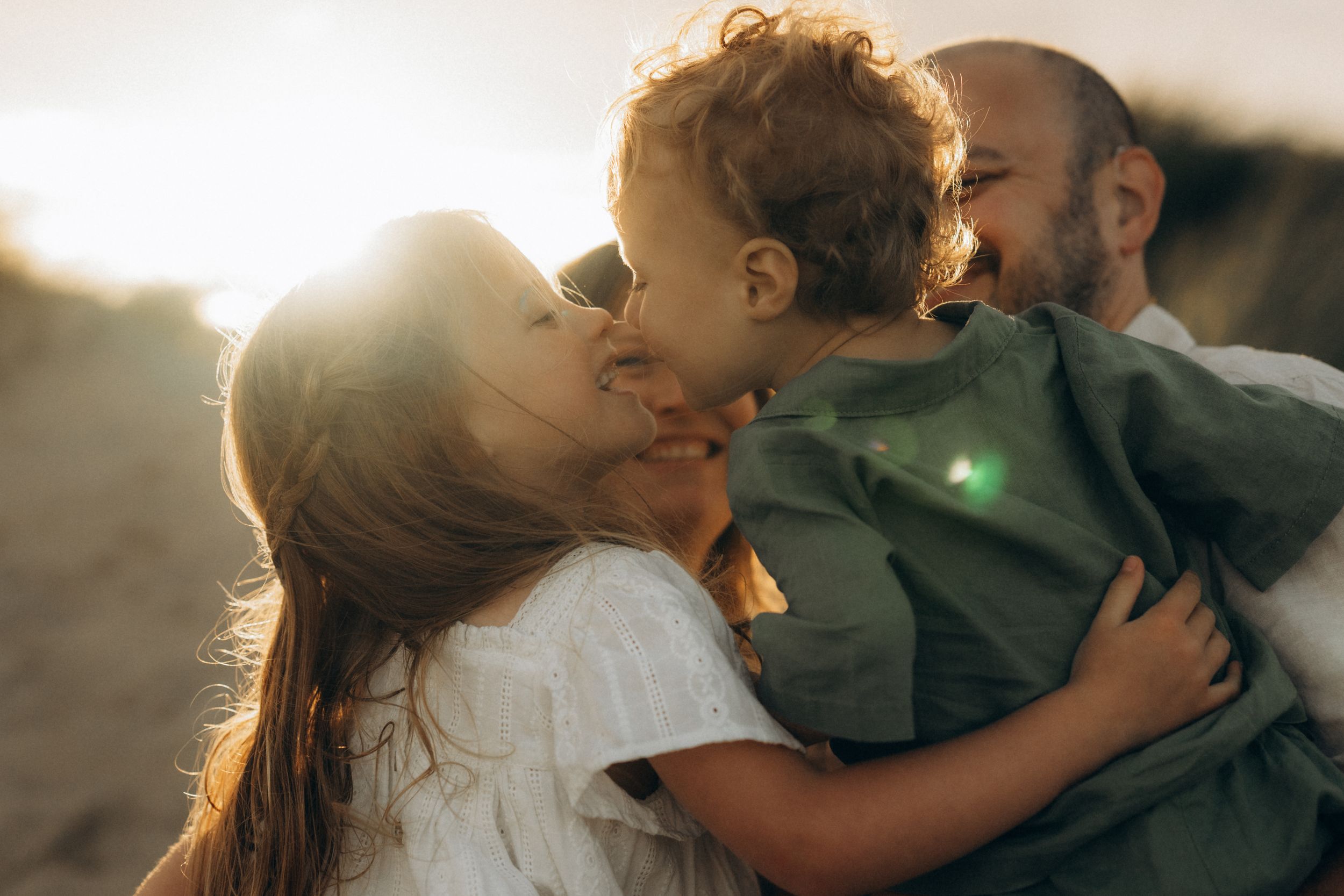 two kids looking at each other gently while being held in their parent's arms at sunset in Camber sands, UK
