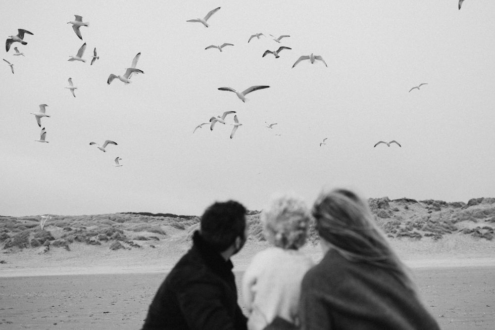 A family of 3 looking at seagulls on the beach during a photo session in Camber sands Kent with family photographer Forever Ours Photography