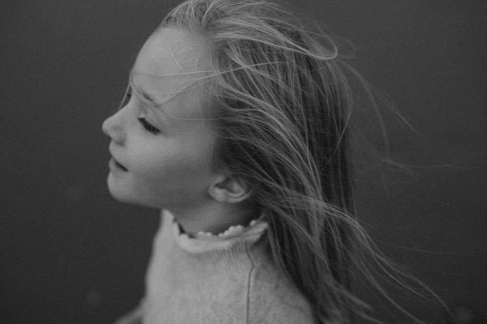 A little girl smiling while her hair is flowing in the wind during a photo session in camber sands