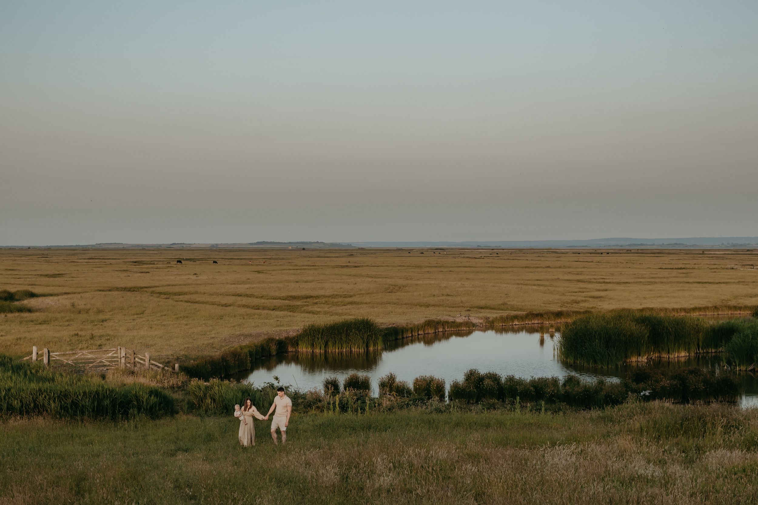 a family of three holding hands and walking through a field a sunset during a family phot session in Kent