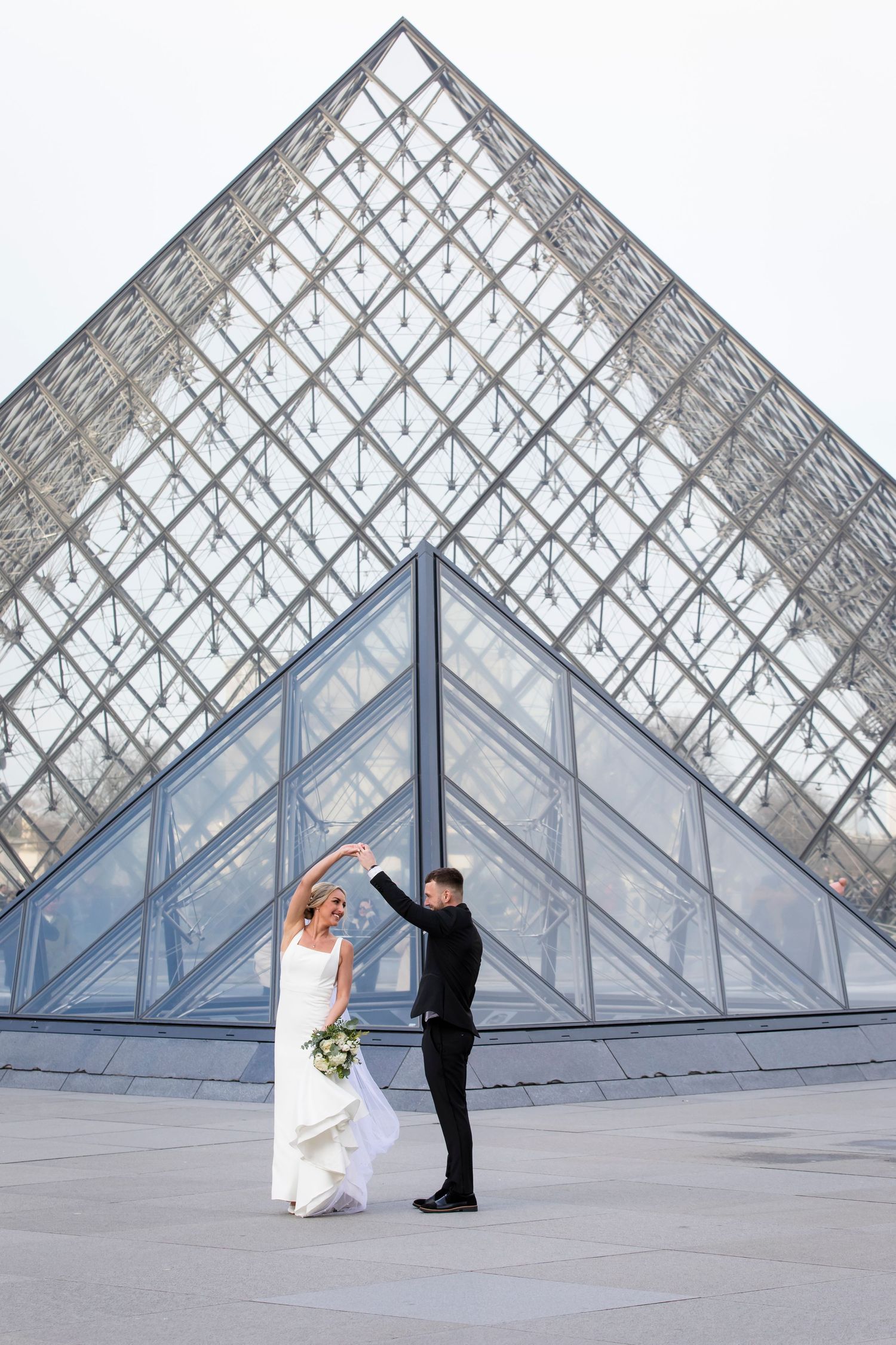 Couple dancing at the Pyramid of the Louvre Museum adds a unique touch to this wedding photo by Julien LB Photography