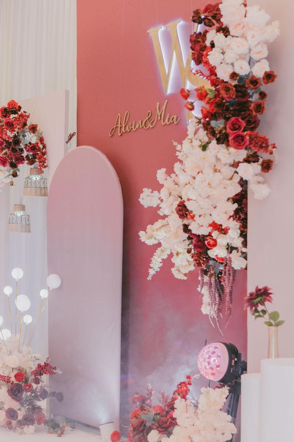Pink wedding backdrop with 'WS' sign decorated with red and white floral arrangements.