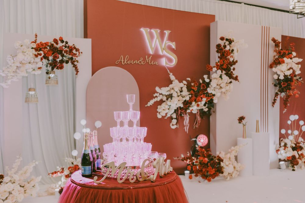 Wedding reception ballroom with red accent wall, floral decorations and tiered cake display.