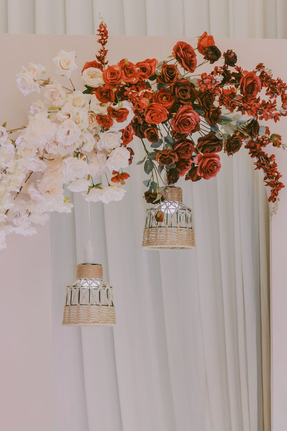 Red roses and white floral arrangements cascading along white-draped wedding backdrop.