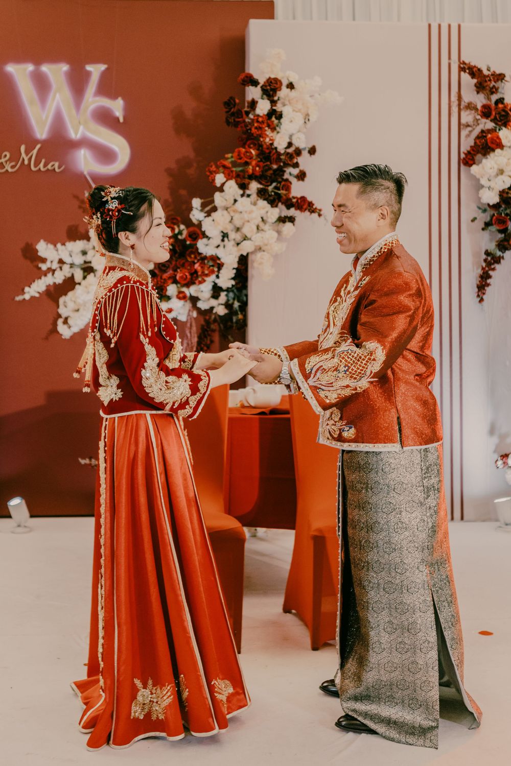 A couple in traditional red Chinese wedding attire exchanging items during ceremony.