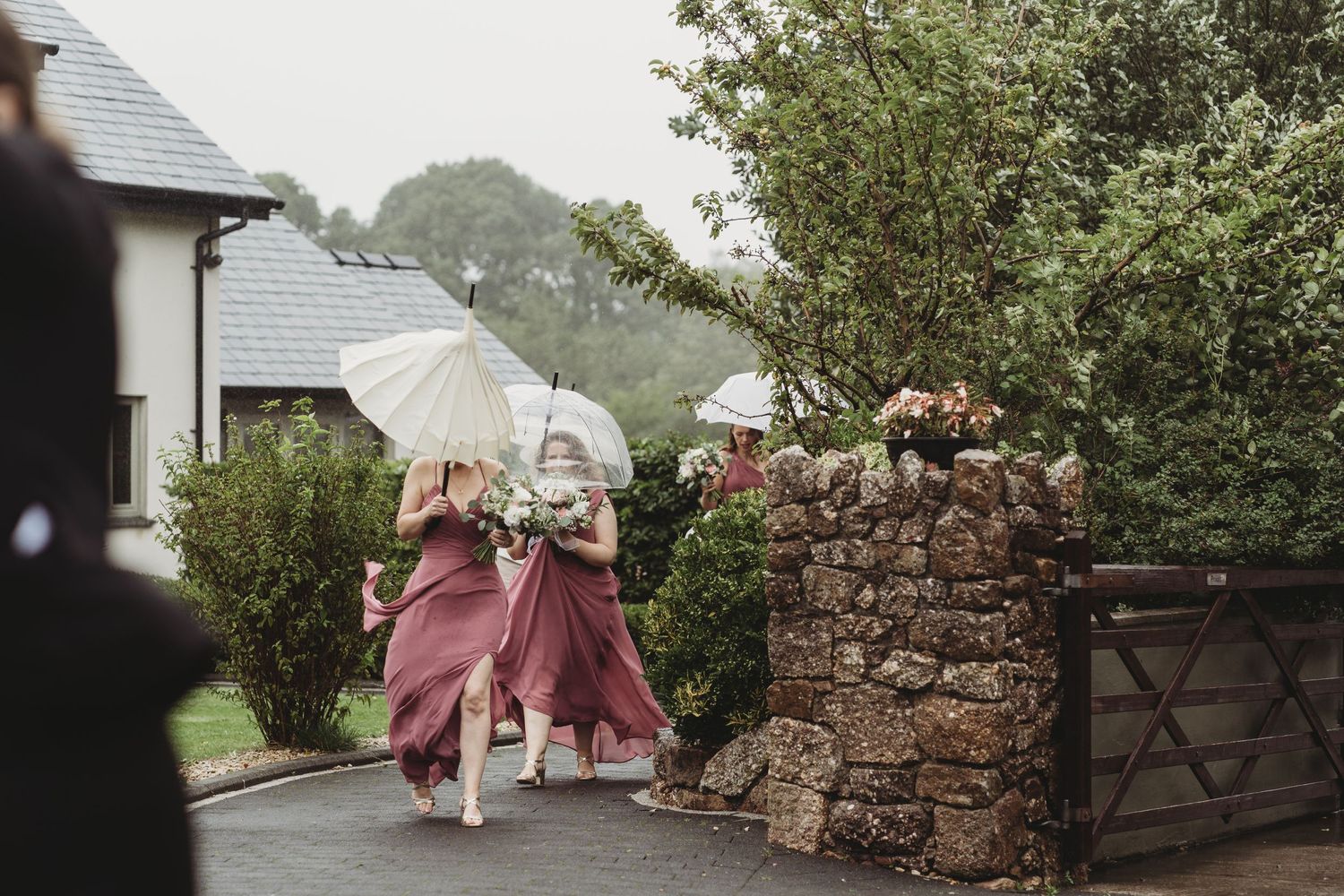 Bridesmaids arriving at a venue with umbrellas blowing in their faces.