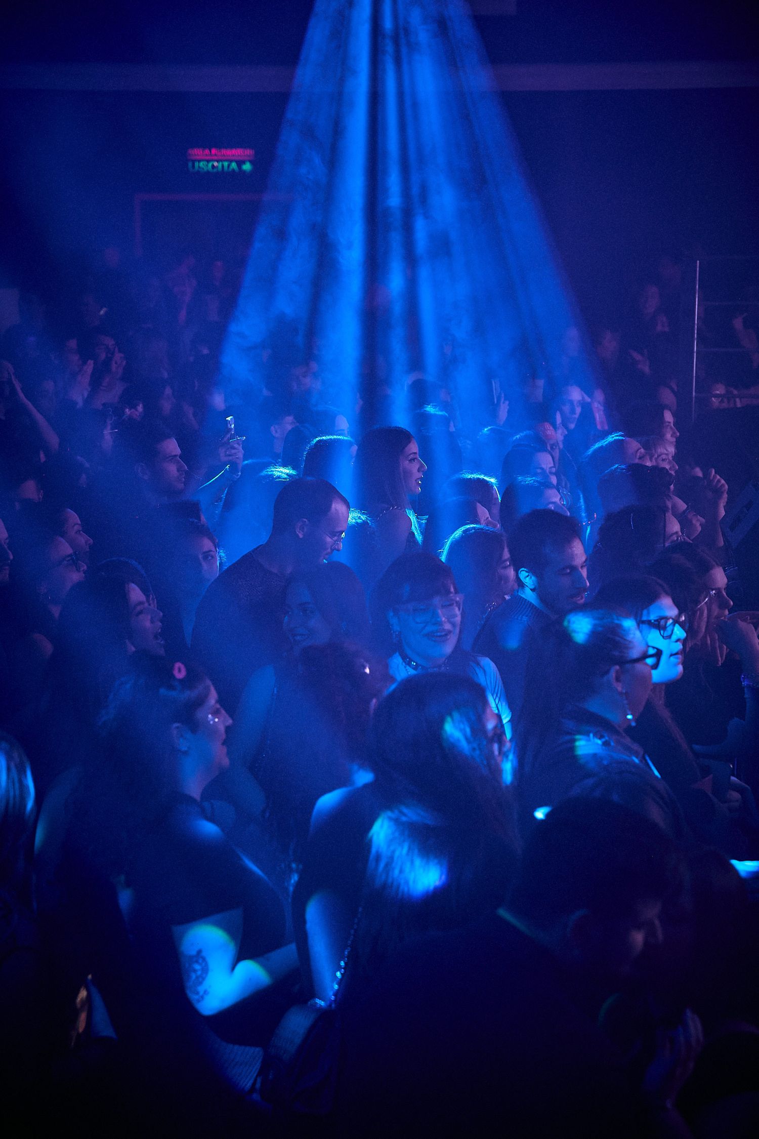 Blue spotlight illuminates crowded nightclub dance floor with atmospheric lighting.