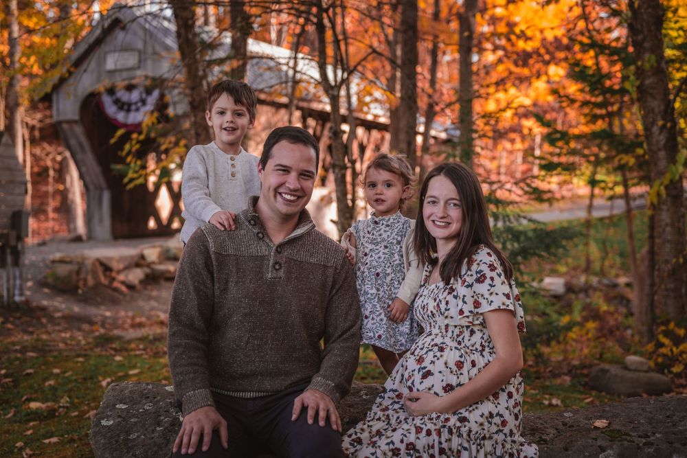 Happy family of four with pregnant mother posing among vibrant autumn foliage.