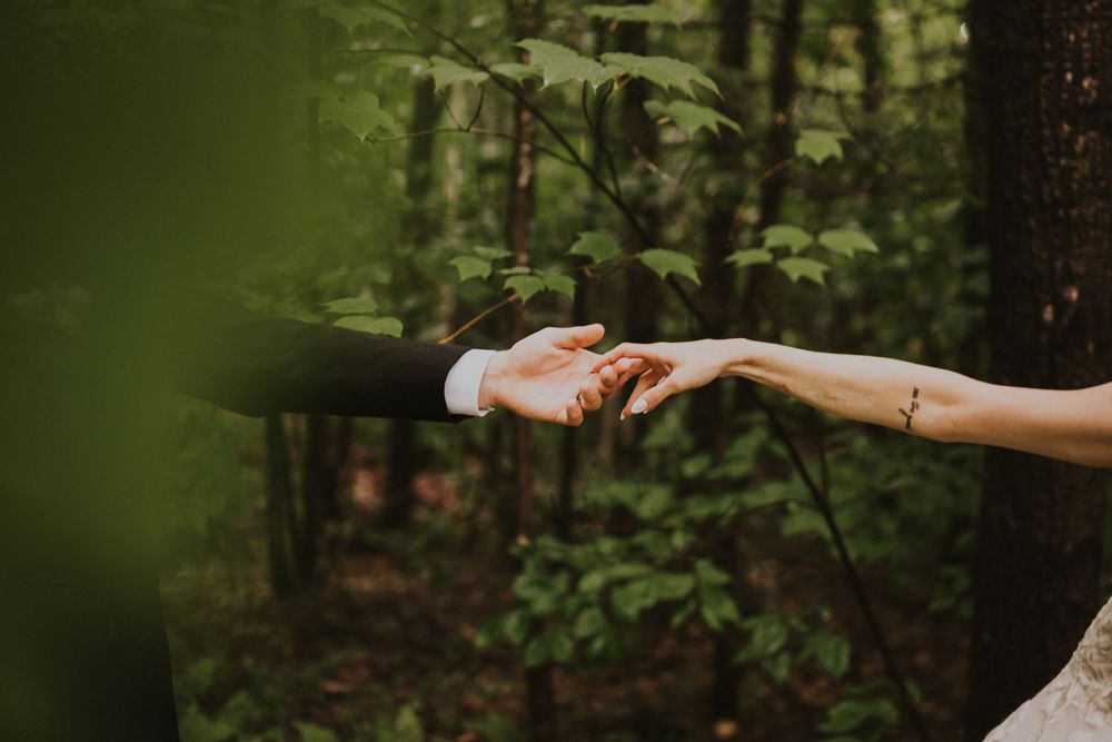 A bride and groom hold hands gently in a lush green forest setting.