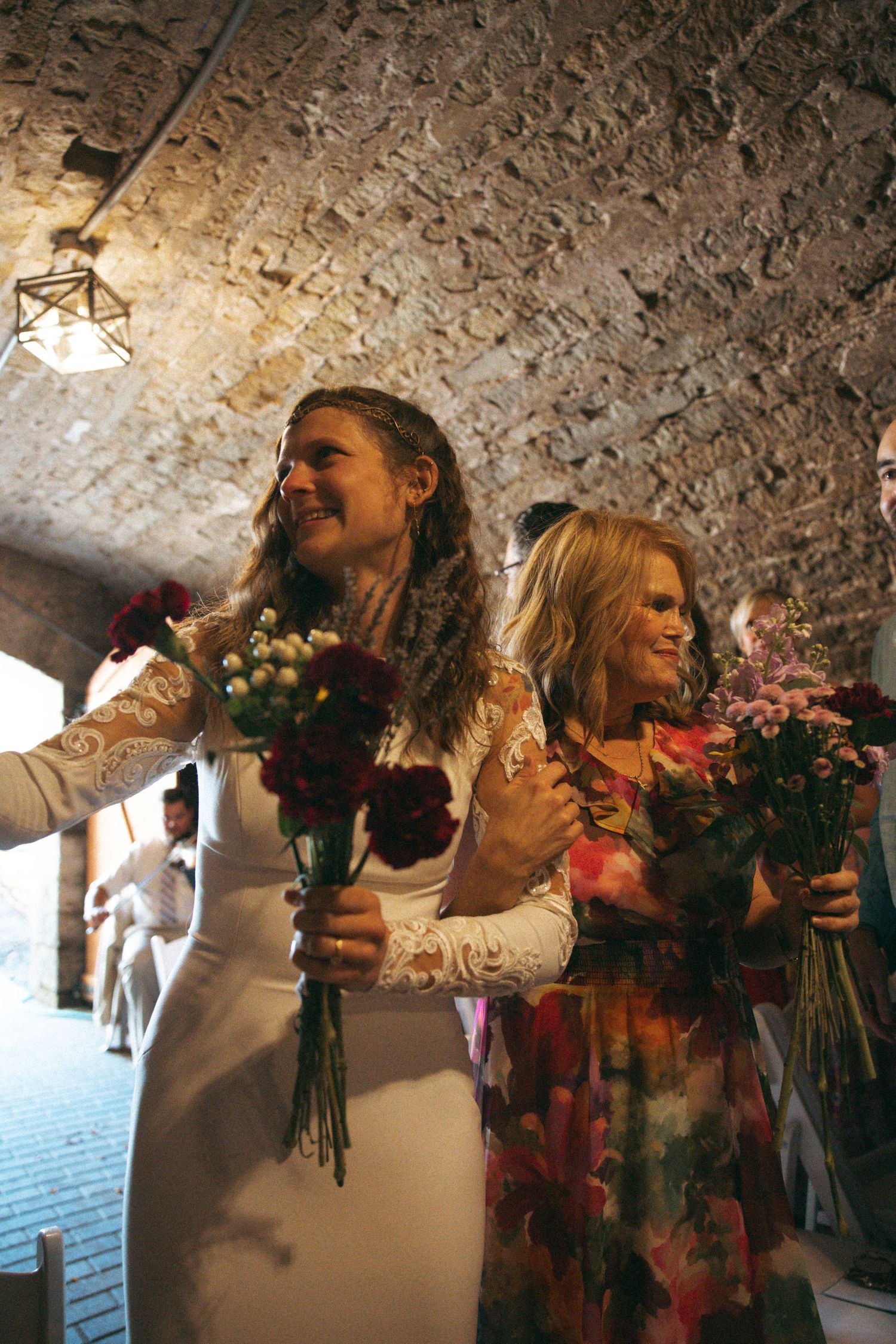 Wedding ceremony in rustic brick cellar with couple holding colorful floral bouquets.