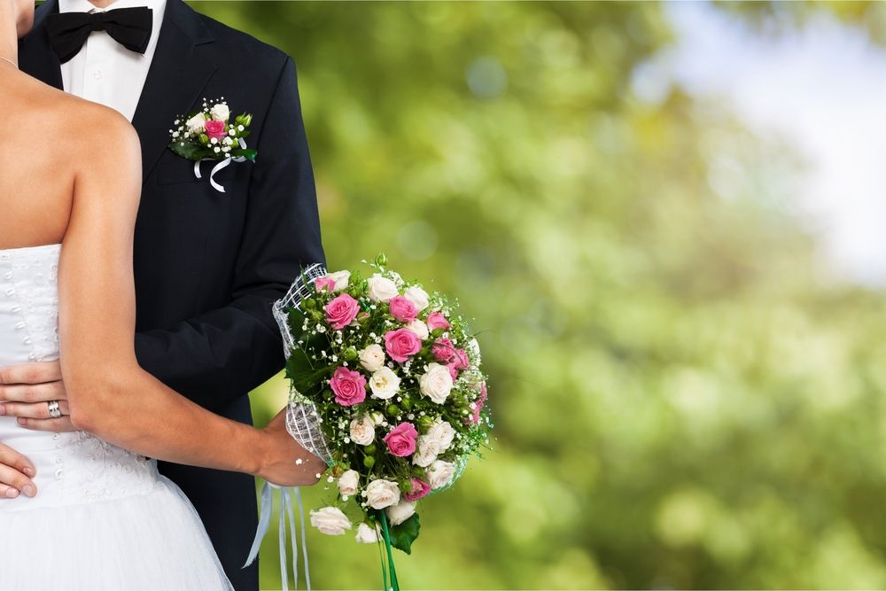 Wedding couple holding a pink and white floral bouquet with formal attire.