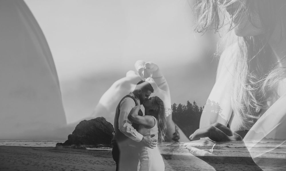 Black and white double exposure photo of a couple kissing on a beach with rocky coastline backdrop.