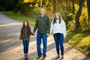Family walking together on a sunlit autumn path through trees with golden light filtering through the foliage.