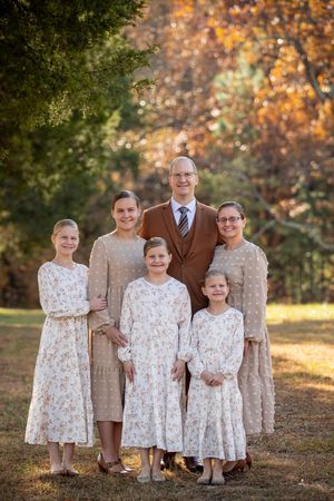 Family portrait in coordinating brown and floral outfits standing together during autumn sunset in a park setting.