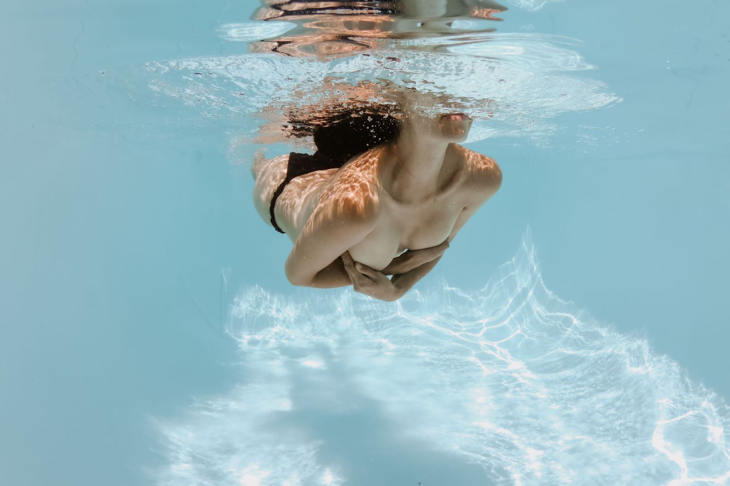 Person in white swimwear gliding underwater in crystal clear turquoise ocean water.