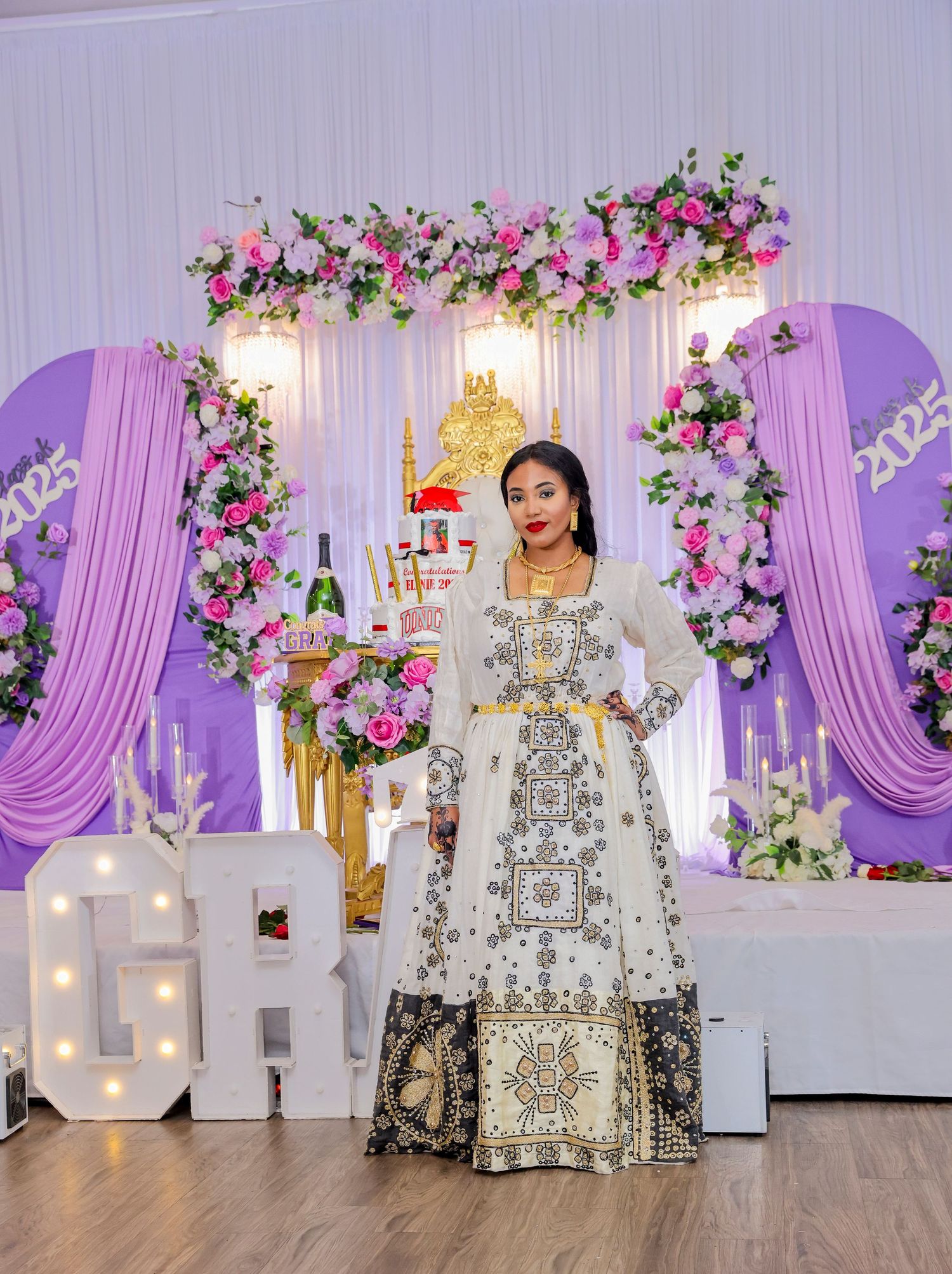 Woman in elegant traditional embroidered gown posing at a lavish 2025 graduation celebration decor.
