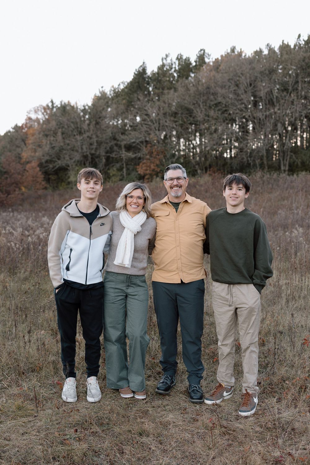 A family group portrait with coordinated neutral outfits against a natural autumn backdrop.
